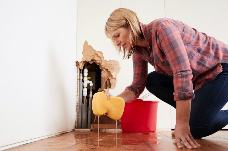Worried woman mopping up water from a burst pipe with sponge
